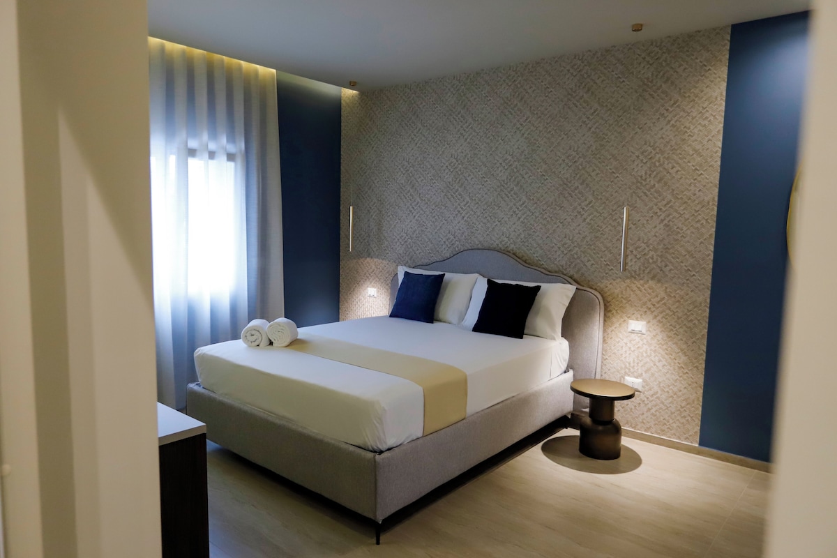 Una habitación de hotel moderna con una cama grande, una mesita de noche y una pequeña mesa junto a la ventana.