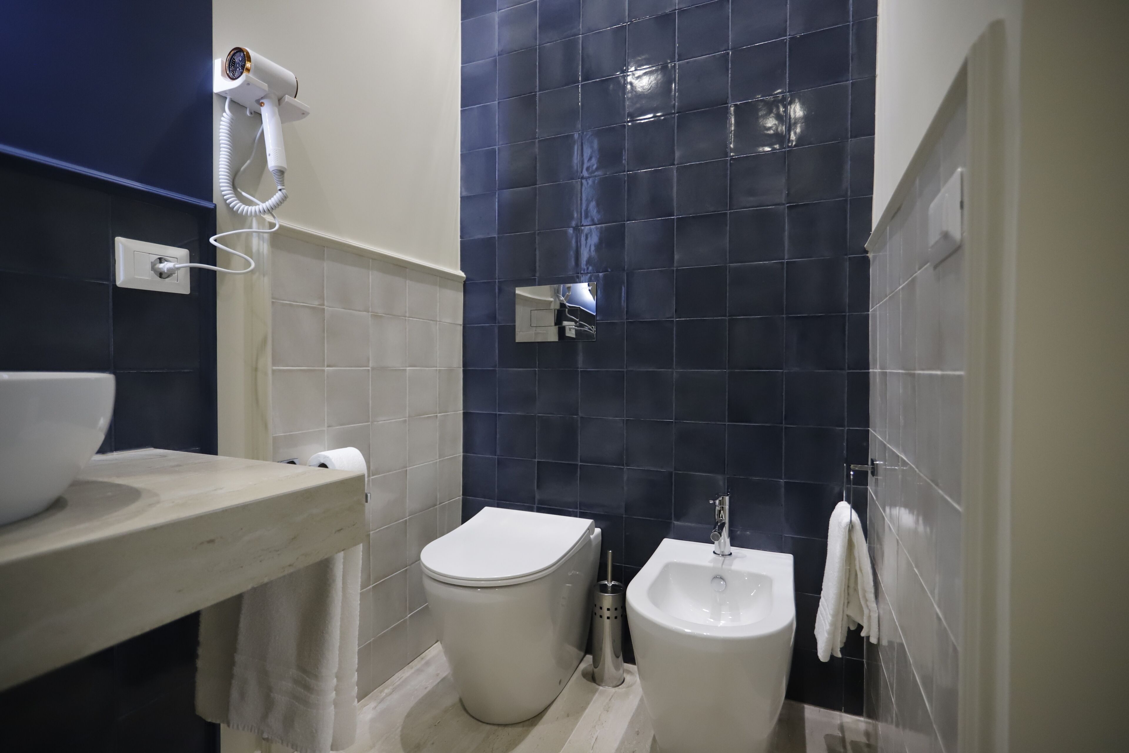 Casa de banho com sanita, bidé e secador de cabelo fixado na parede.
