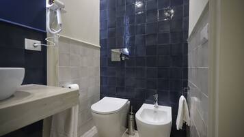 Casa de banho com sanita, bidé e secador de cabelo fixado na parede.