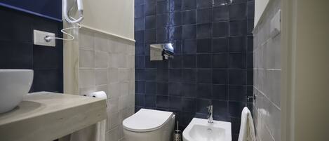 A bathroom with a toilet, bidet, and a hairdryer mounted on the wall.