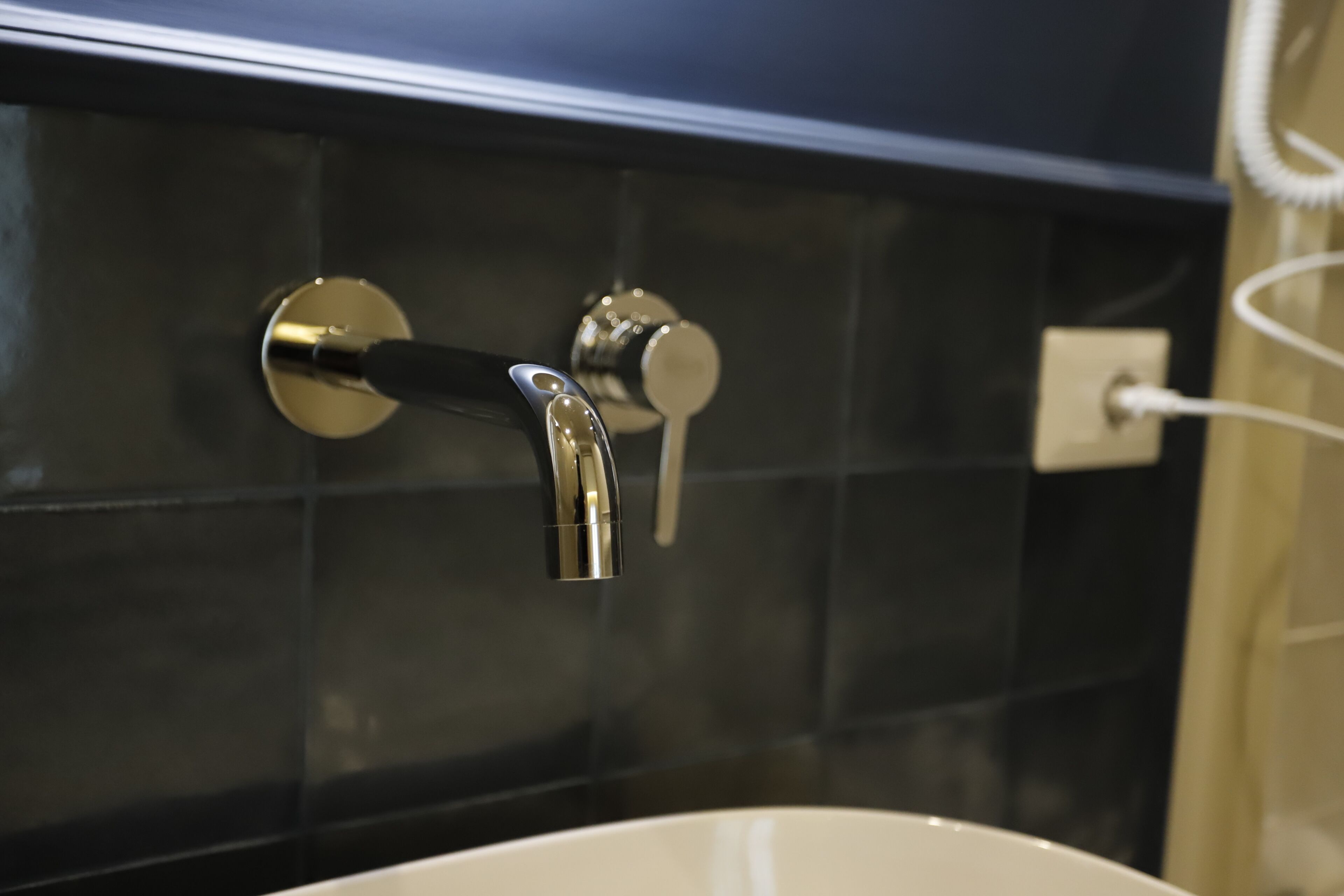 A bathroom with a white sink, a chrome faucet, and a wall-mounted light switch.