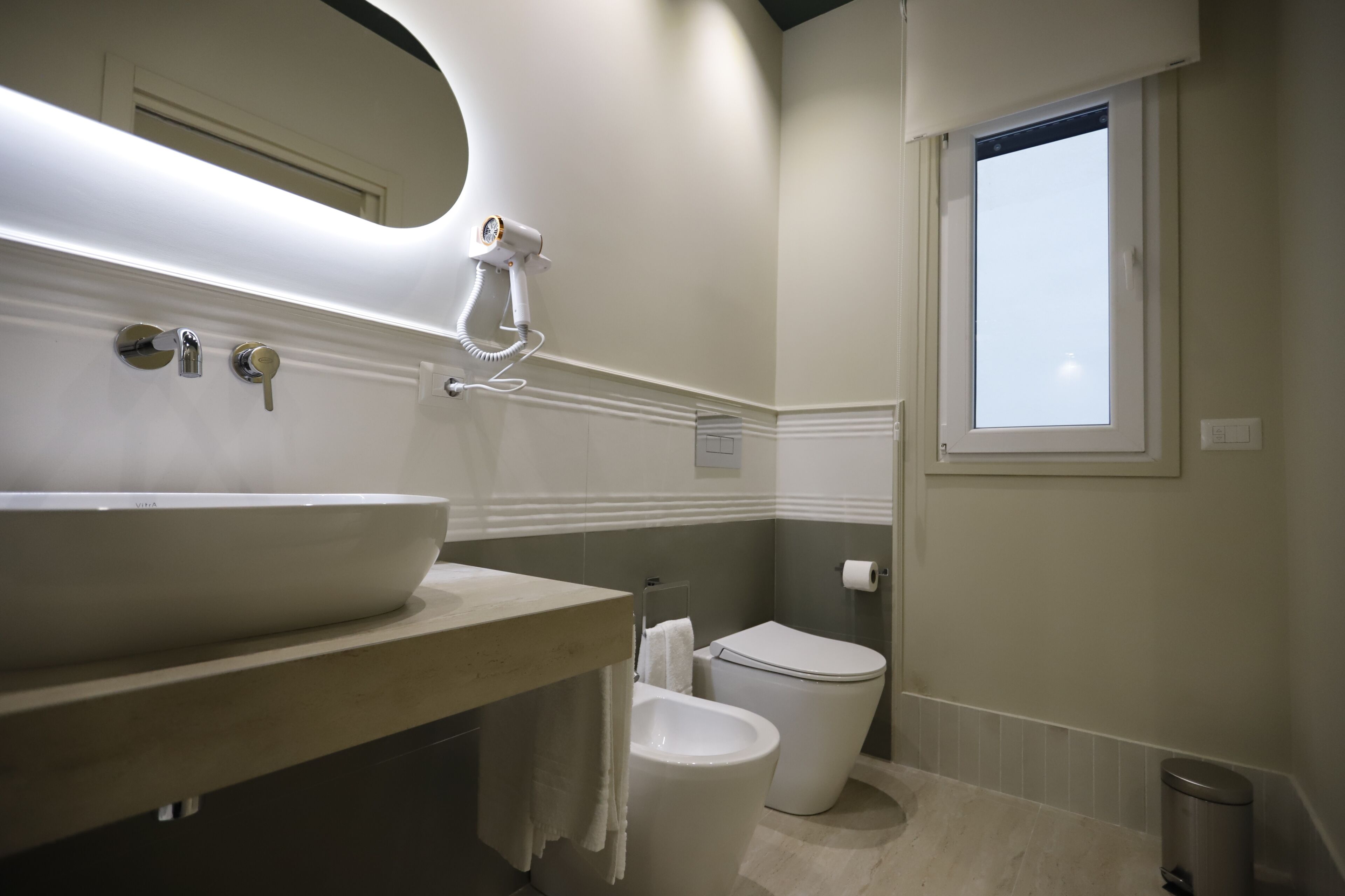 A bathroom with a large sink, toilet, and a window.