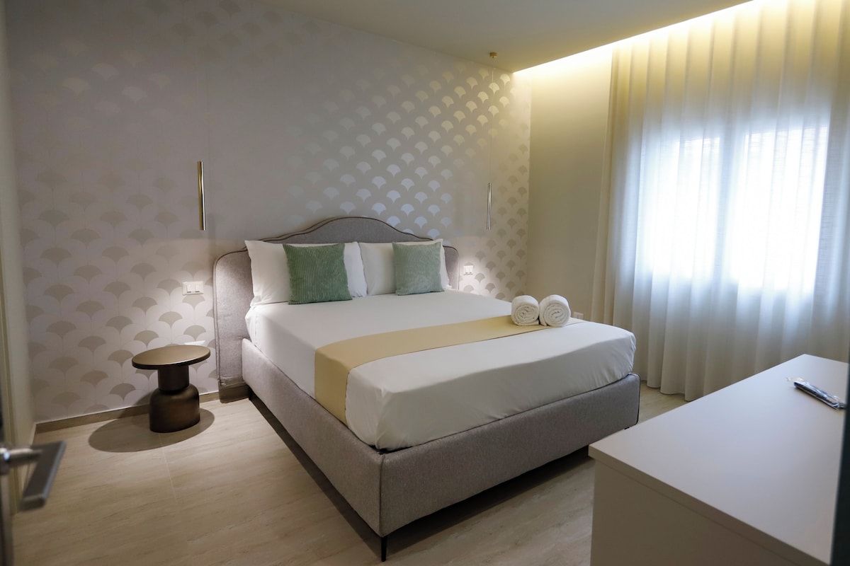 Una habitación de hotel ordenada con cama, mesita de noche y un pequeño escritorio.