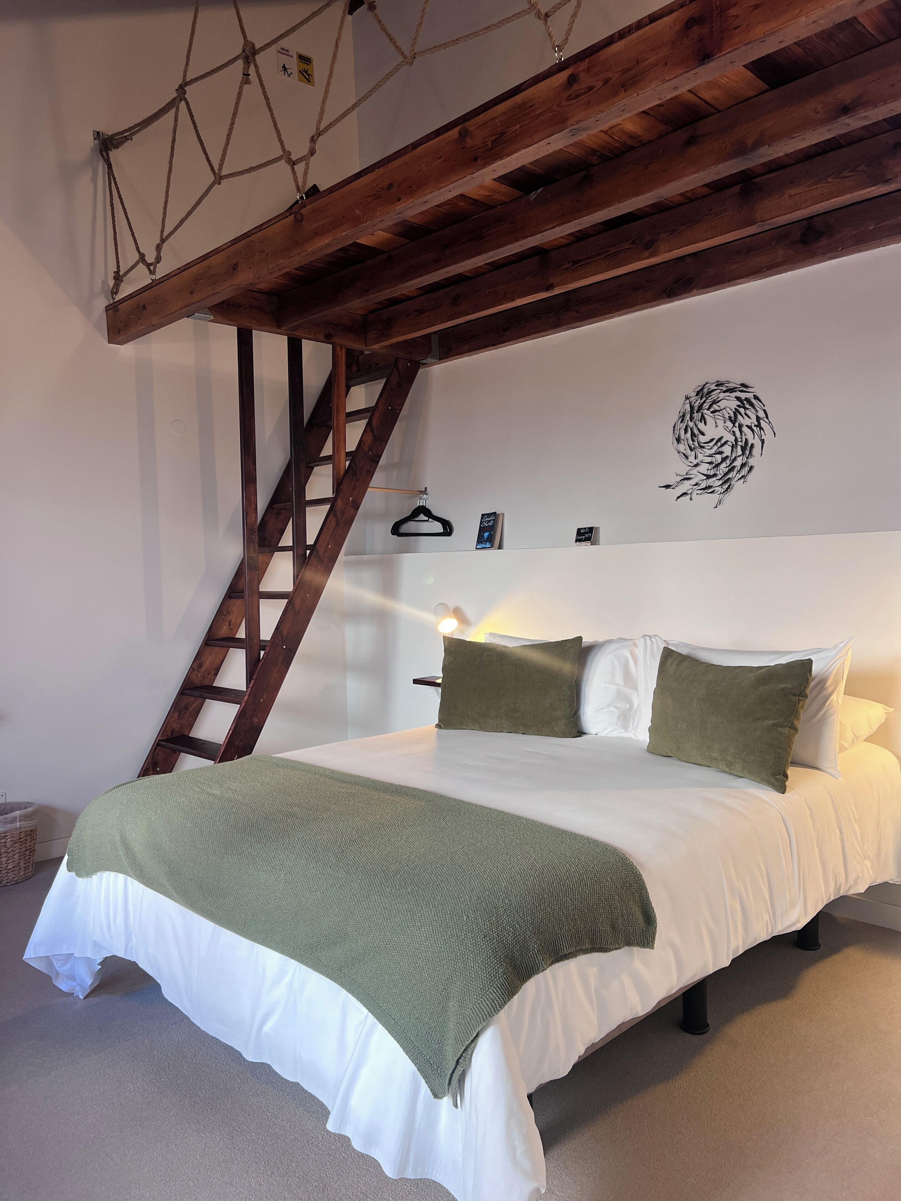 A bed with a white and green bedspread, a wooden ladder, and a wall-mounted light fixture.
