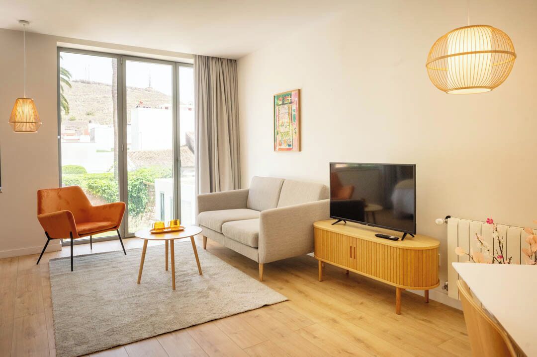 Un salon moderne avec un canapé, un fauteuil, un téléviseur et un meuble en bois.