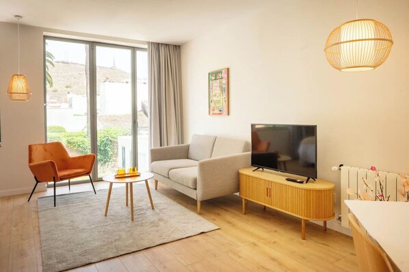 Una sala moderna con un sofá, un sillón, televisión y un mueble de madera.
