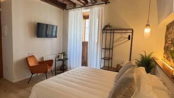A bedroom with a wooden ceiling, a bed with white bedding, a chair, a TV, and a plant.