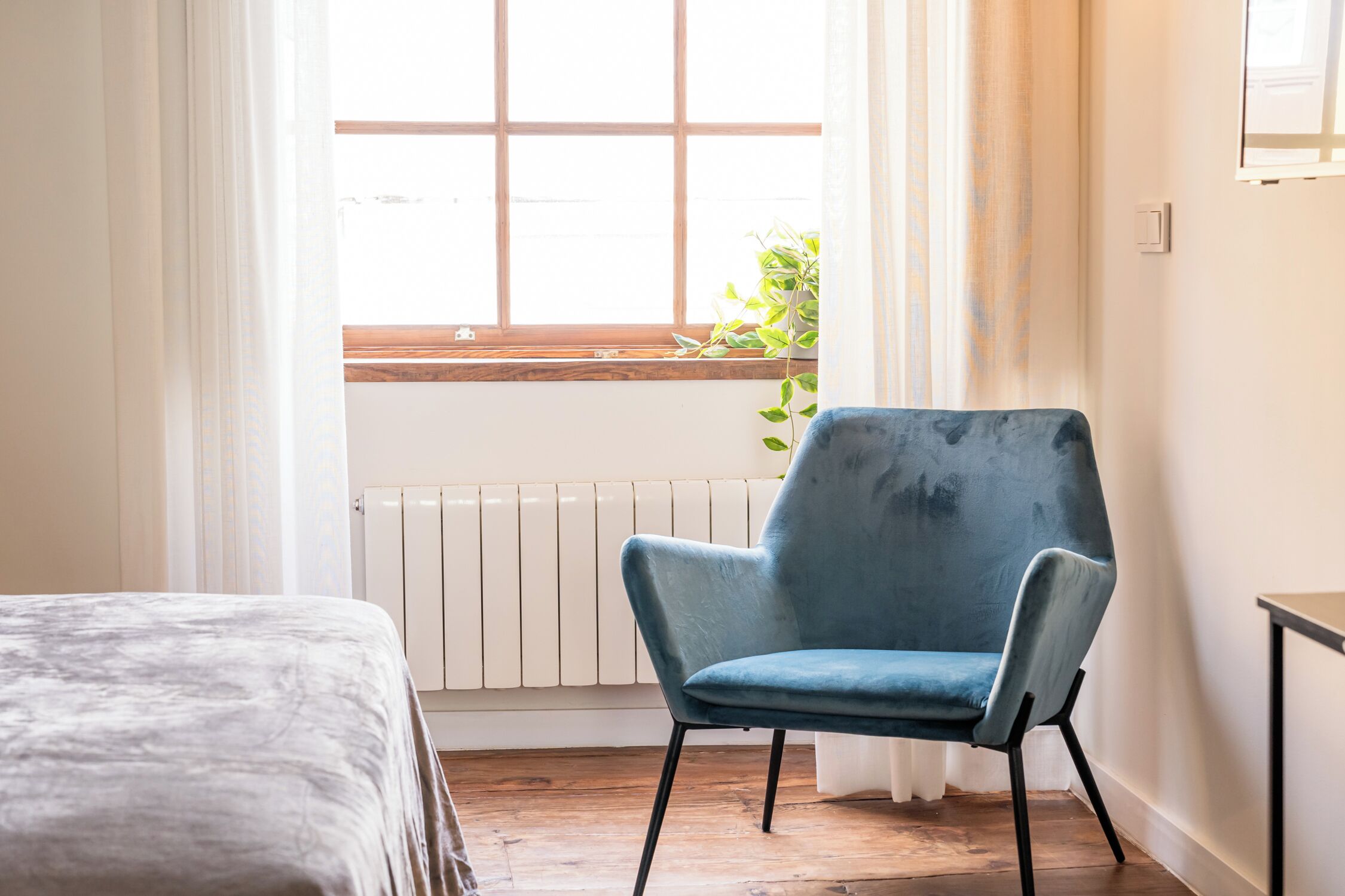 A room with a bed, a blue chair, a window with a view, and a radiator.