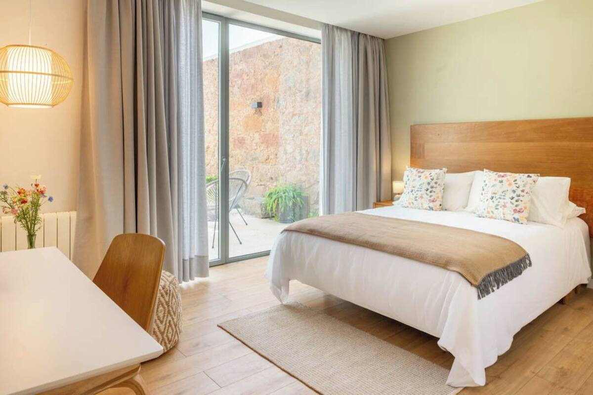 Habitación de hotel con cama, una silla, una mesa y vistas a un espacio exterior.