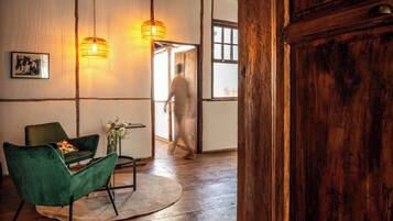 Ein Zimmer mit Holzboden, einem grünen Sessel, einem Tisch mit einer Vase und zwei Hängeleuchten.