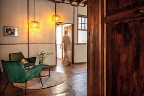 A room with a wooden floor, a green chair, a table with a vase, and two hanging lamps.