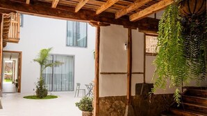 Un espace patio extérieur agrémenté d’un mur en pierre, de poutres en bois, d’une plante suspendue et d’un petit jardin avec un palmier.