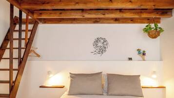 A bedroom with a wooden ceiling, a bed with two pillows, a wall-mounted light, a small plant, and a wooden ladder.