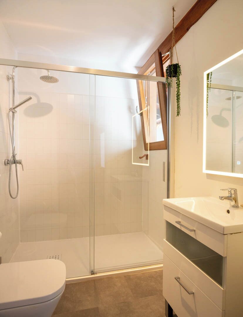 Un baño moderno con ducha de vidrio, lavamanos blanco y espejo.