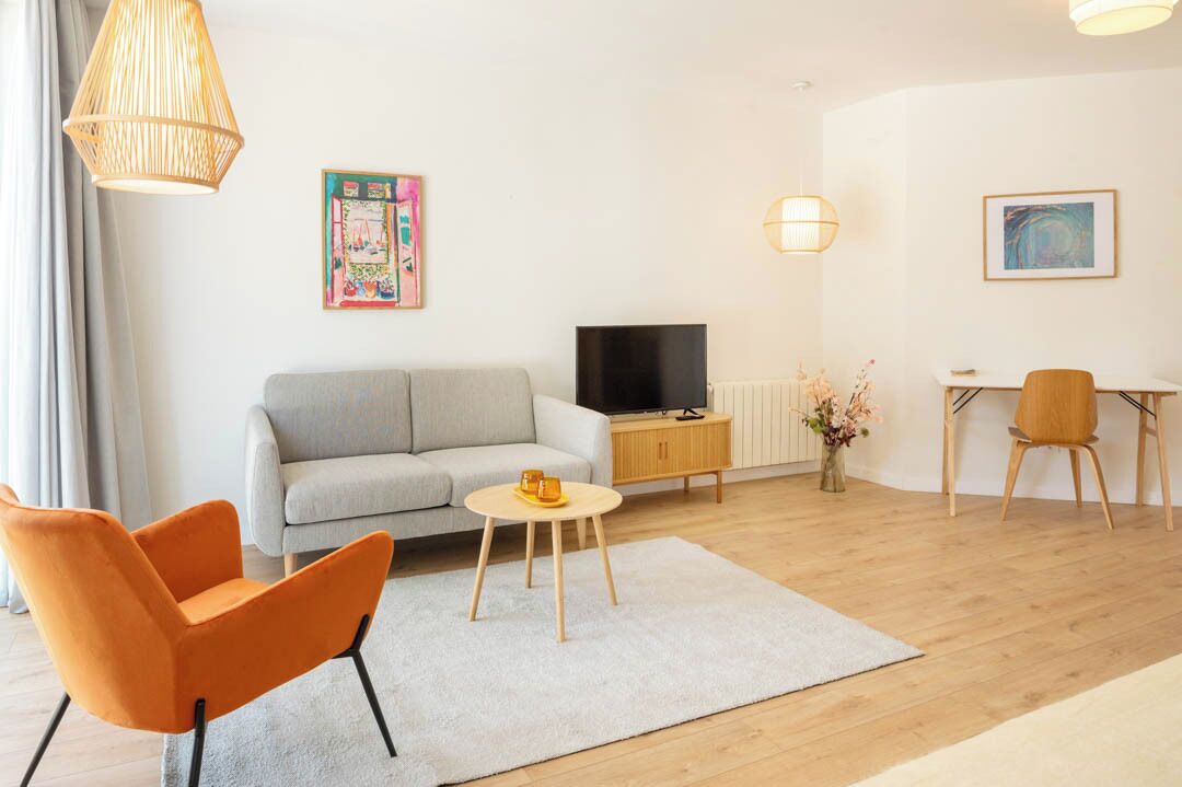 A modern living room with a sofa, TV, orange chair, round coffee table, and artwork on the walls.