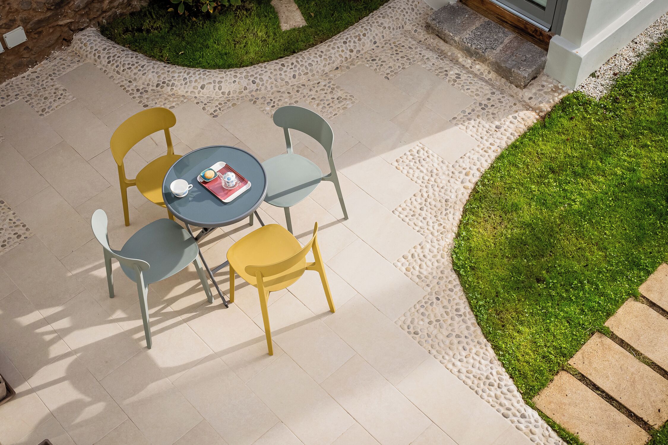 Une terrasse avec une table ronde et quatre chaises, entourée d’une bordure de galets et d’une zone herbeuse.