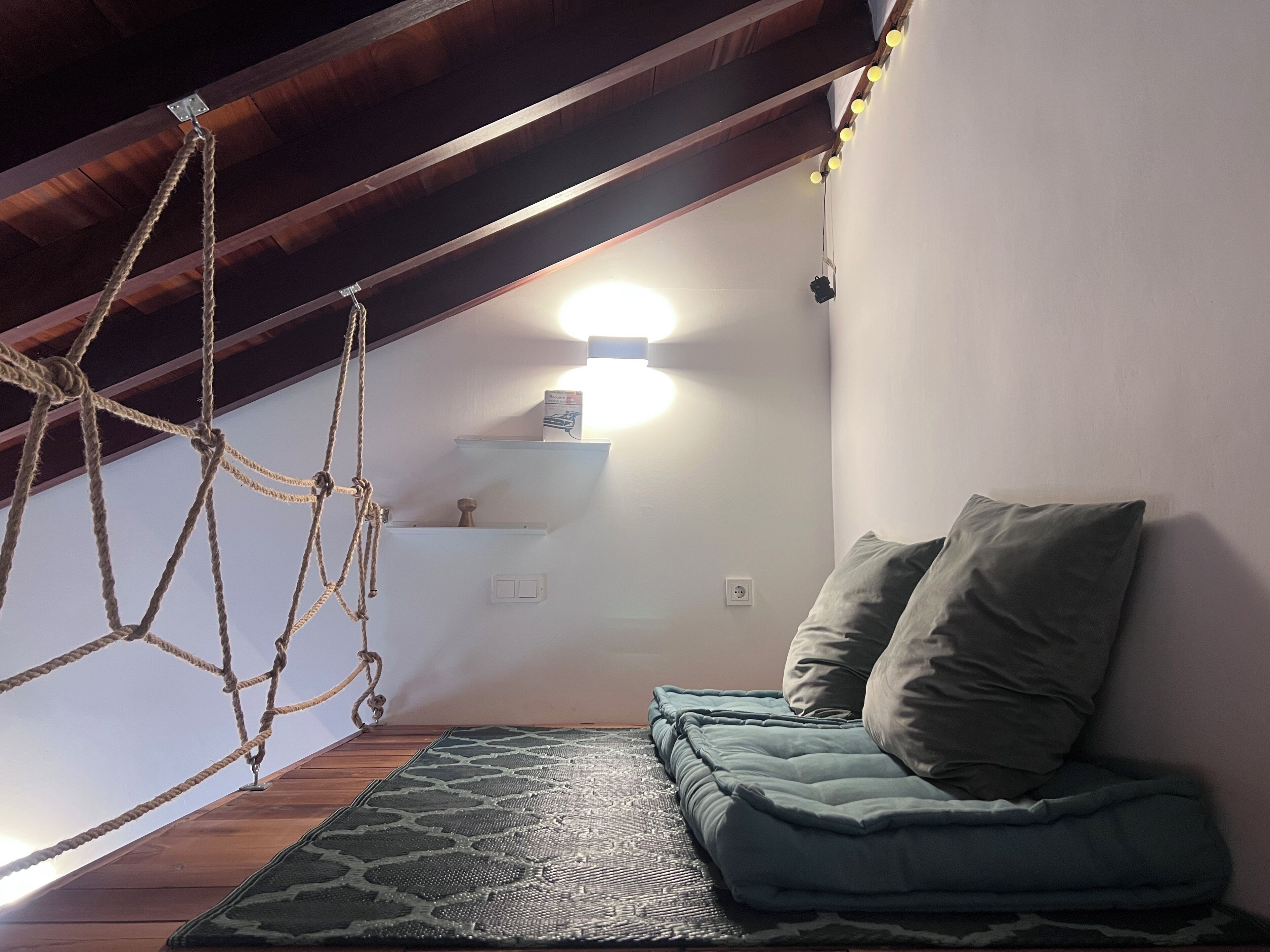 A loft bedroom with a hanging rope swing, a green sofa, and a wall-mounted light fixture.