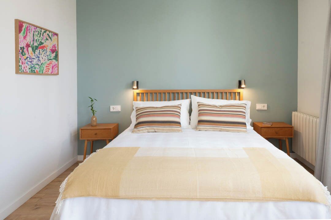 A neatly made bed with striped pillows, a bedside table with a lamp, and a wall-mounted artwork.