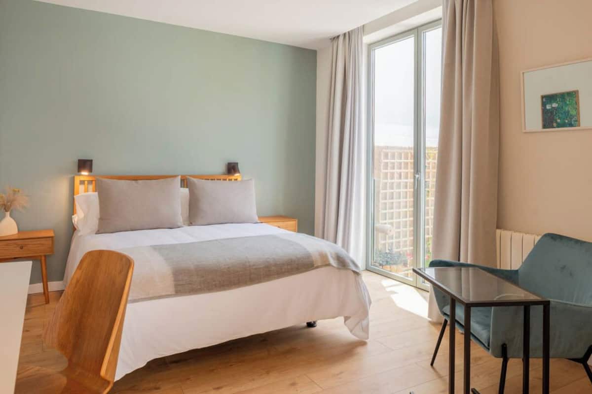 Un dormitorio con una cama, una silla, una mesa y una ventana con cortinas.