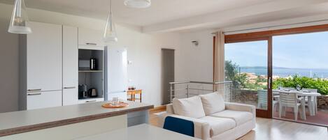 Een moderne keuken met witte kasten, een eethoek met een witte tafel en stoelen, en een balkon met uitzicht op het landschap.