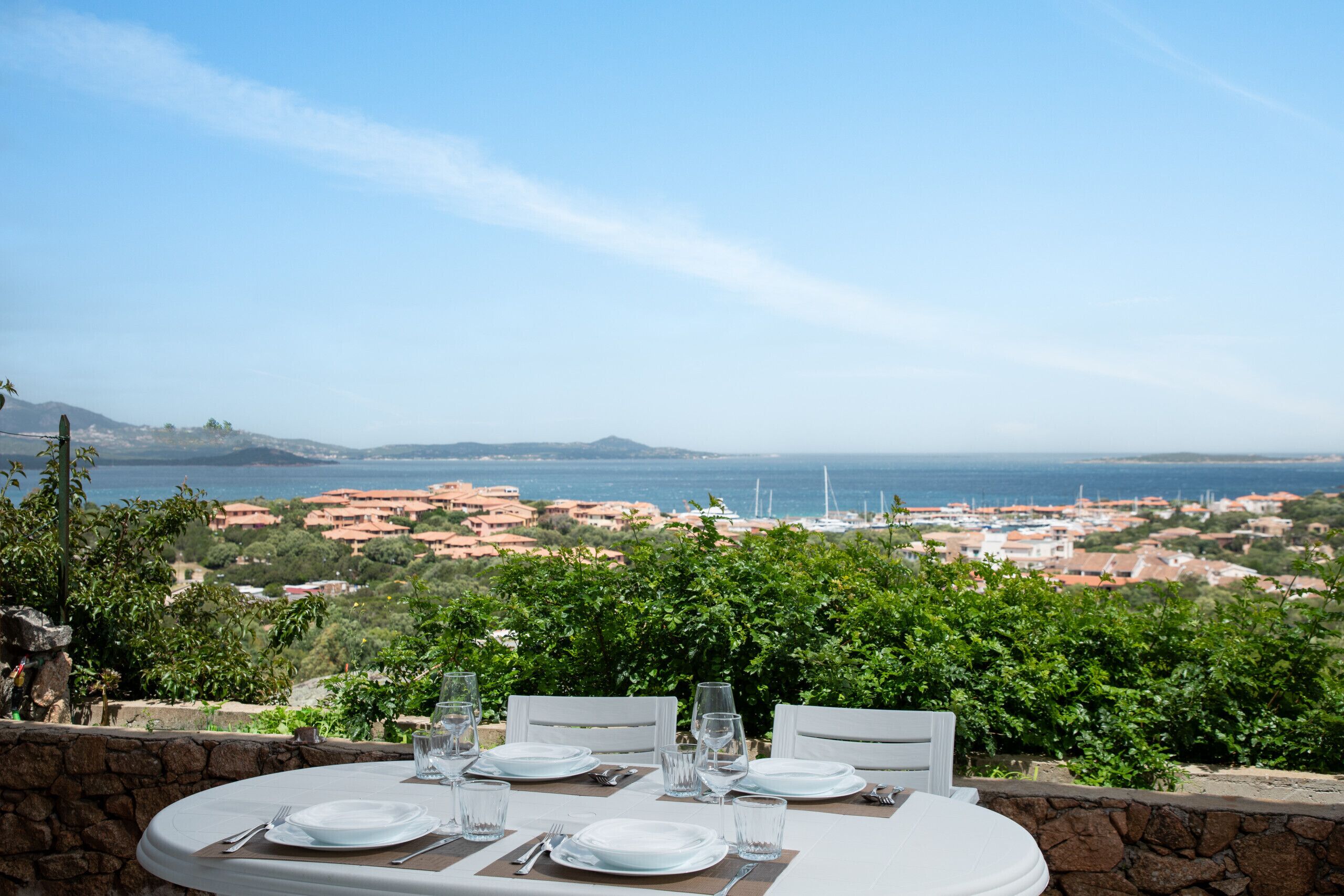 A table set for dining with a scenic view of the sea and buildings in the distance.