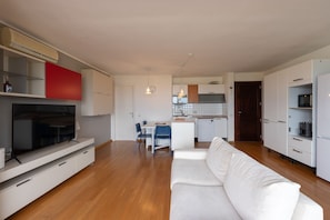 Ein modernes Wohnzimmer mit einem Flachbildfernseher, einem weißen Sofa und einem Essbereich mit Tisch und Stühlen.