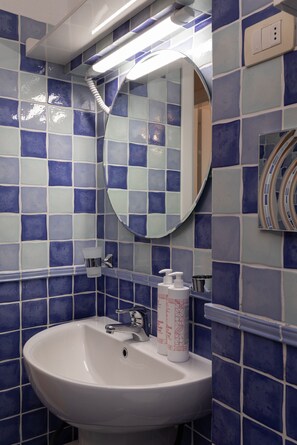 Um banheiro com pia branca, azulejos azuis e brancos, espelho e secador de mãos.