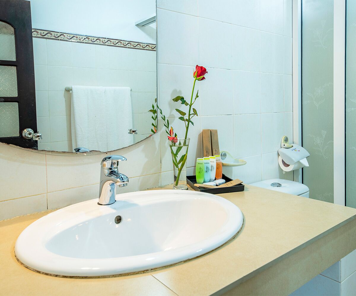 Ein Badezimmer mit einem weißen Waschbecken, einem Spiegel, einem Handtuchhalter, einer Toilette und einem Glas mit einer roten Rose.