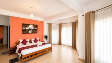 A hotel room with a bed, a fan, a painting, and curtains.
