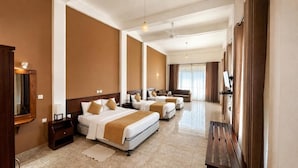 Habitación de hotel con tres camas, un espejo grande, un banco de madera y vistas a la ciudad.