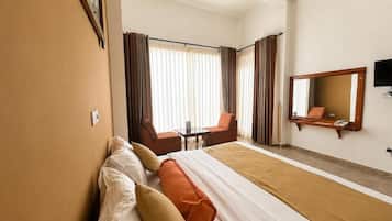 Quarto de hotel com uma cama, duas cadeiras, uma mesa, uma televisão e um espelho grande.