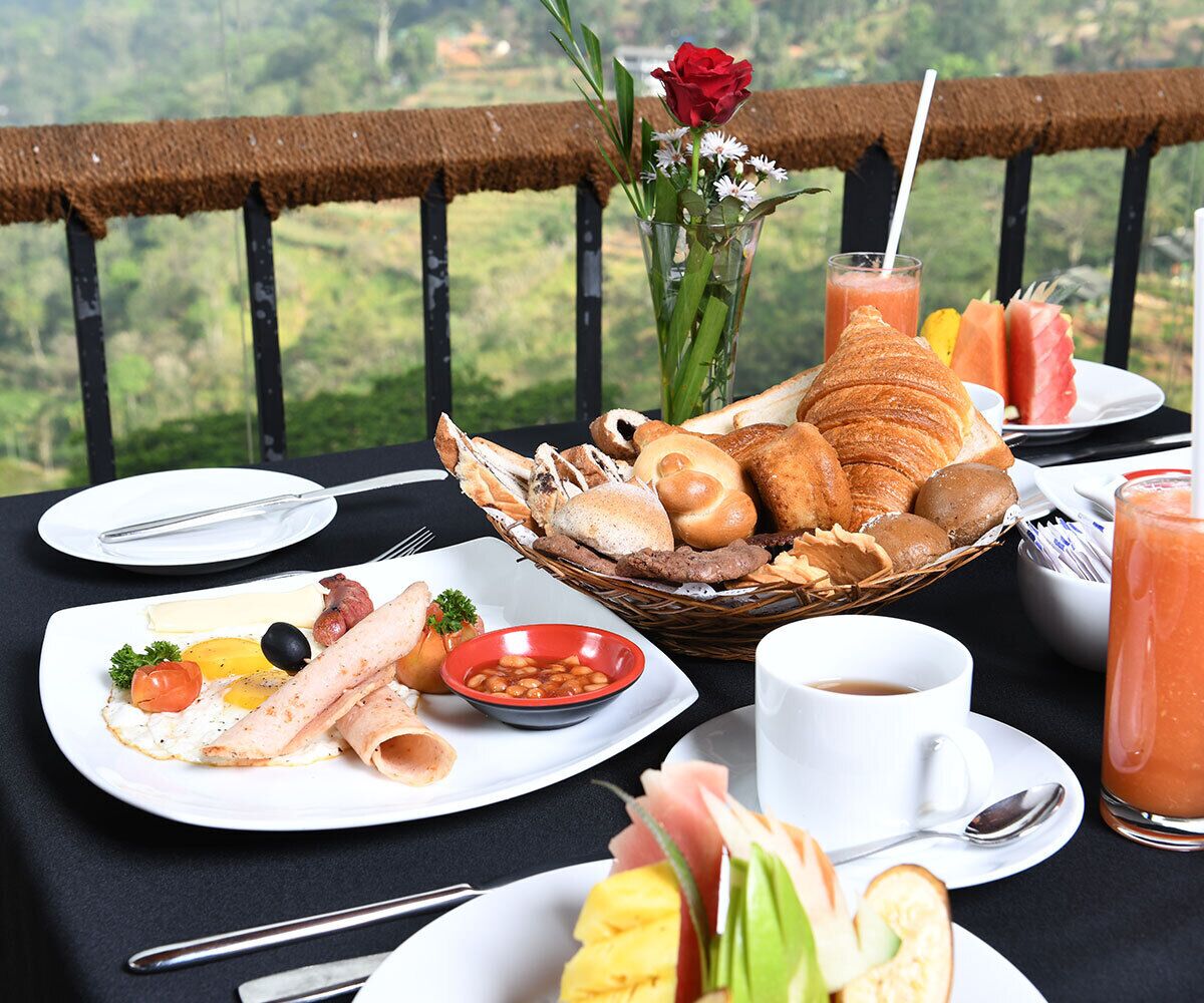Una mesa de desayuno con cruasanes, pan, un bol de frijoles y un plato con huevos, tomates y jamón.