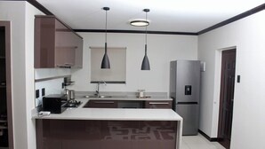 Una cocina moderna con una isla central, luces colgantes, horno empotrado y refrigerador.