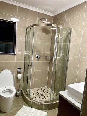A bathroom with a glass-enclosed shower, a toilet, and a sink. - The Cozy Maison (Midrand)