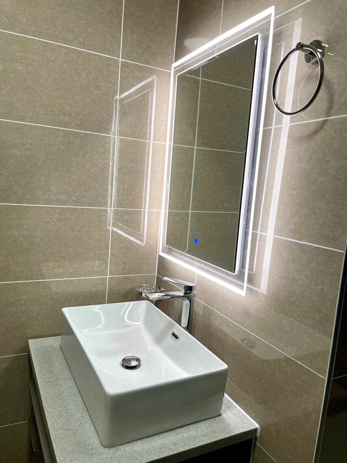 Une salle de bain avec un lavabo blanc, un robinet chromé et un miroir doté d’une bande lumineuse.