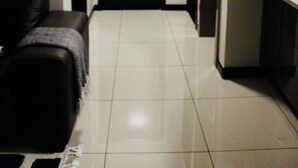 Un pasillo con una puerta negra, piso de baldosas blancas, un sofá negro y una pequeña cocina con armarios y encimera.