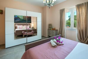 Ein Schlafzimmer mit einem Bett, einem Schminktisch, einem Spiegel, einem Nachttisch und einem Fenster mit Vorhängen.