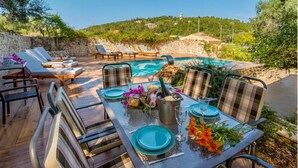 Un espace extérieur aménagé pour les repas, avec une piscine, des murs en pierre et des chaises longues.
