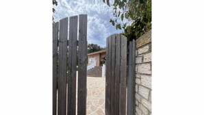 Une porte en bois mène à un sentier pavé de pierres et à un bâtiment doté d’un mur en pierre.