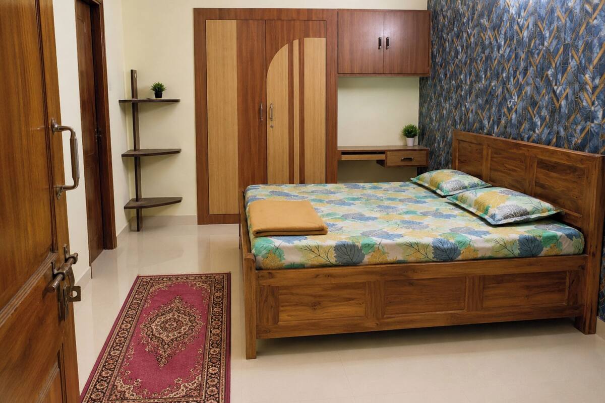 A bedroom with a wooden bed, a wardrobe, a desk, and a patterned wall.