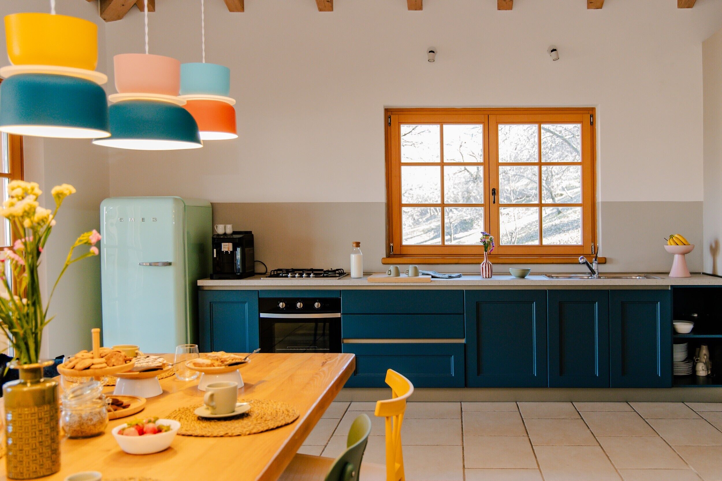Eine Küche mit Holztisch, blauen Schränken und einem Fenster mit Blick auf Bäume.