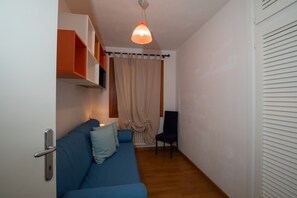A room with a blue sofa, a chair, a hanging light fixture, and a door with a handle. - Casa Ald a Manna by Wonderful Italy (Olbia)