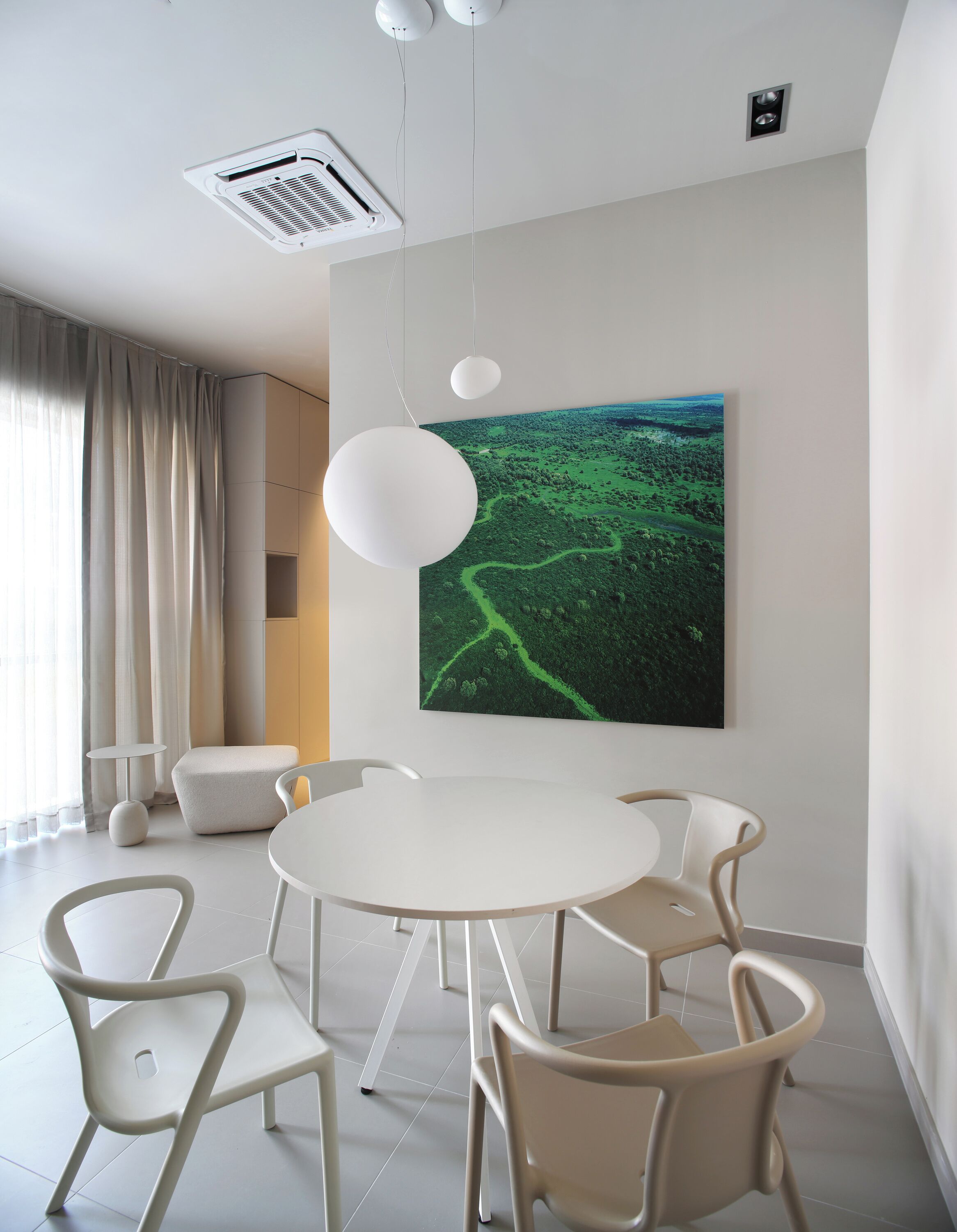 A modern dining area with a round table, six chairs, a large green landscape painting, and a ceiling vent.