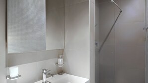 Un baño moderno con un espejo grande, un lavamanos blanco y una zona de ducha con mampara de vidrio.