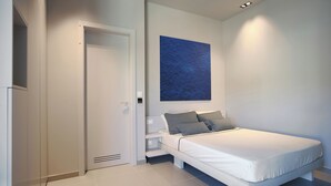Un dormitorio con cama, mesita de noche, una obra de arte en la pared, una puerta y una lámpara.