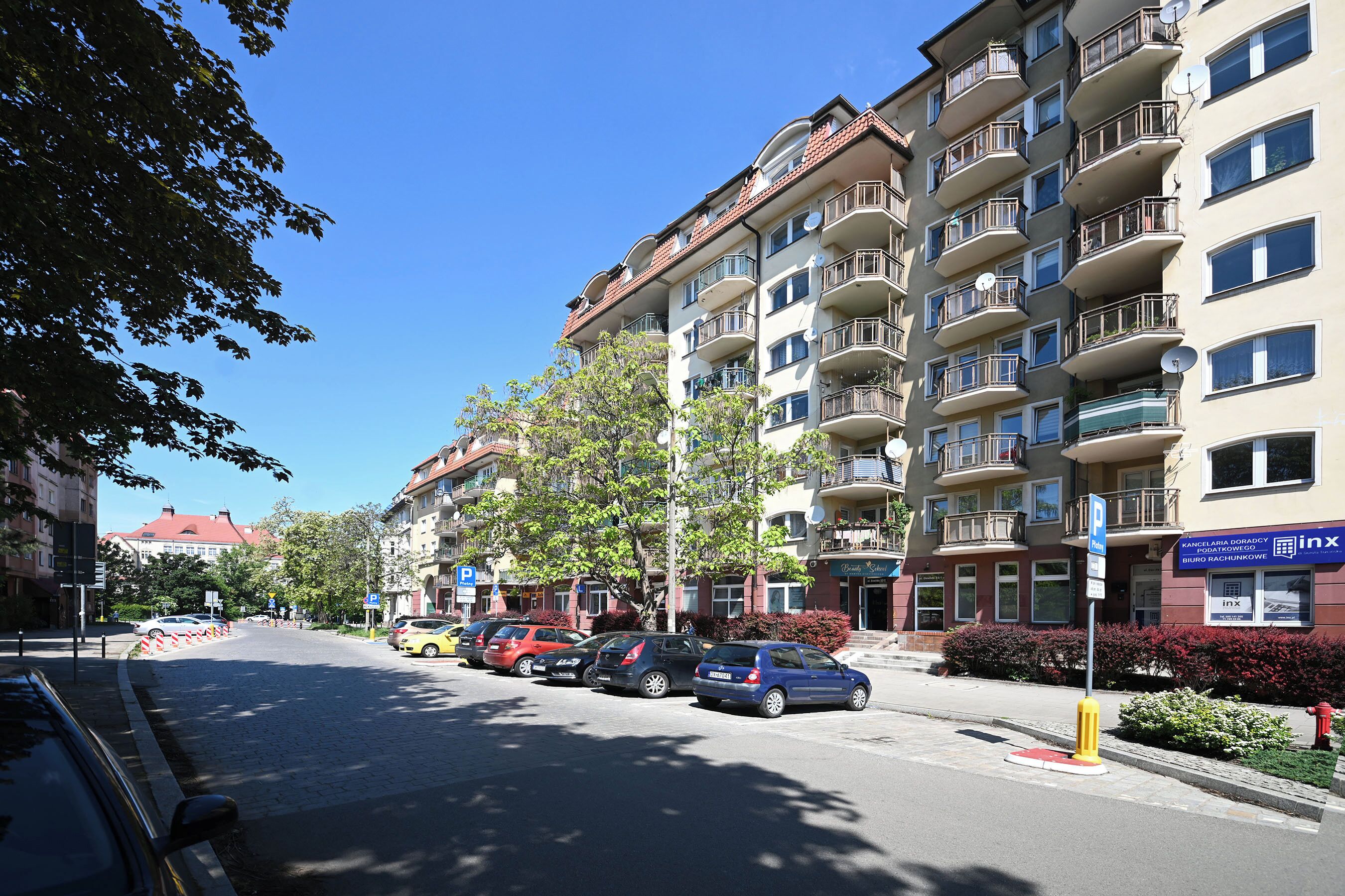 Un immeuble résidentiel à plusieurs étages, doté de balcons, d’un espace de stationnement et surplombant un ciel d ’un bleu éclatant.
