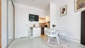 Una cocina moderna con armarios blancos, un televisor de pantalla plana y un comedor con mesa y sillas.