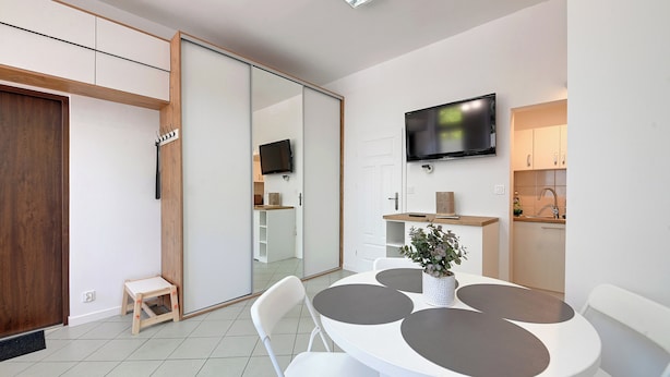 Una habitación moderna con una mesa de comedor, sillas, televisión y una zona de cocina.