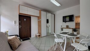 Una sala de estar moderna con un sofá, una mesa de comedor con sillas, un televisor y una puerta corrediza que da a la cocina.