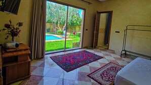 A hotel room with a large sliding glass door leading to a pool, a bed, a desk with a lamp, and a ceiling light. - Perfect 2-bedroom Villa with Pool in delightful Ourika (Ourika)